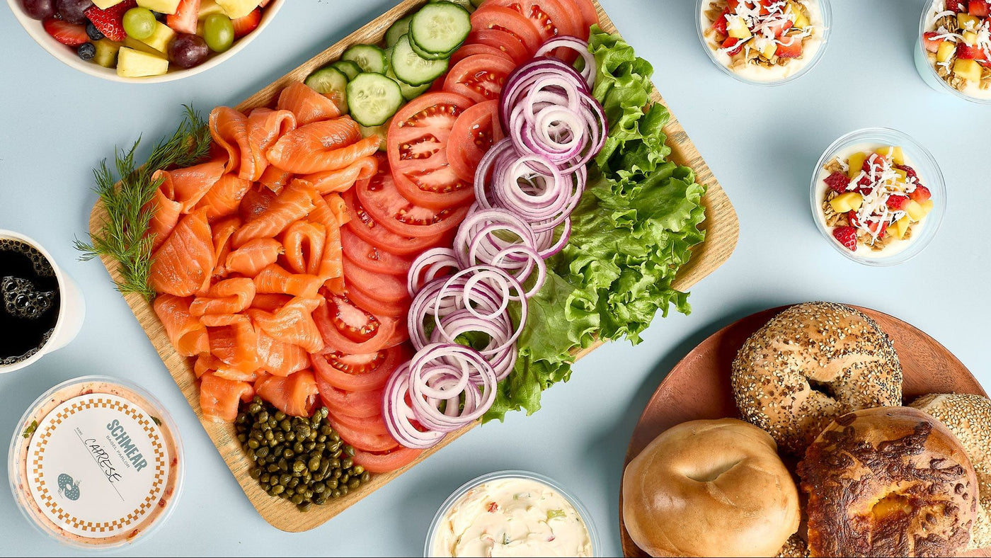 A Schmear Bagel Parlor catering spread with lox, sliced tomato, red onion and capers, bagels, schmears, fruit salad and coffee
